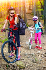 Fototapeta na wymiar Bikes cycling family. Happy mother and daughter wearing helmet are cycling on bicycles into forest. Parenting. Color tone on shiny sunlight background.