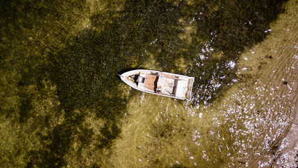 Aerial view of a small wooden fishing boat moored in a shallow, tropical lagoon