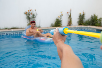 Young friends shooting with water guns at each other while having fun in pool.  