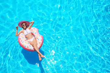 Beautiful young woman with inflatable donut in blue swimming pool - obrazy, fototapety, plakaty