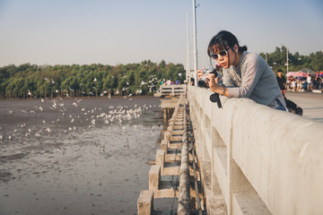 Asian woman with camera standing on the concrete bridge waiting for sunset in Bang pu seaside, Thailand.