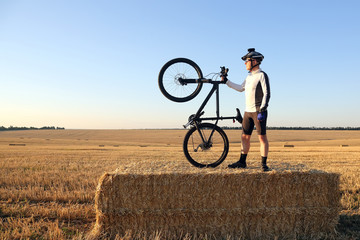 cyclist with the bike resting on straw harvested field
