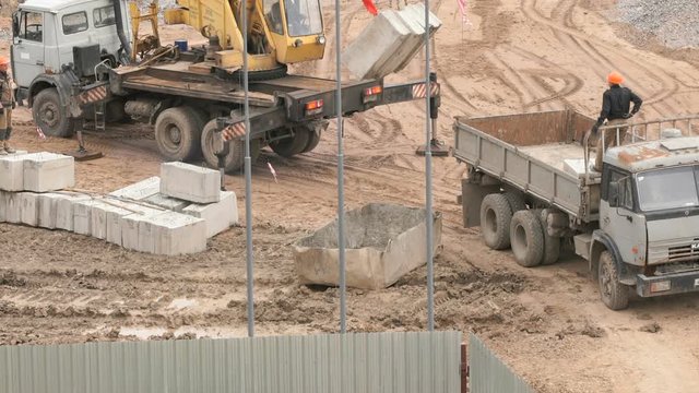 Builder dressed in orange helmet provides uploading of foundation blocks on the dump truck. Construction site