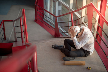 Engineer or Architect feeling tired and headache with his job. sitting on building stairs with...