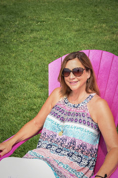 Happy Woman Sitting In Pink Adirondack Chair Outside