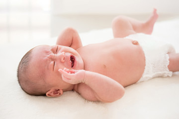 Shirtless newborn baby lying and crying on the bed