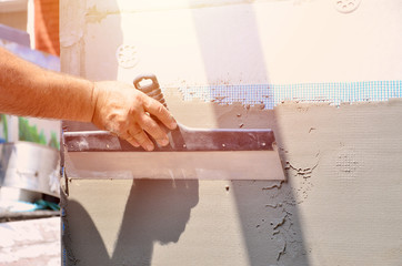 Hands of an old manual worker with wall plastering tools renovating house. Plasterer renovating...