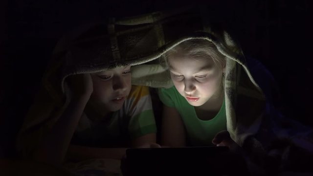 Boy and girl playing with laptop under the covers