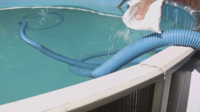 Male hand pouring chemicals out of white sachet into a swimming pool
