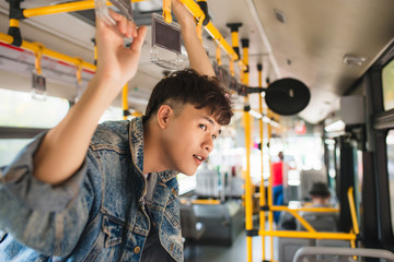 Asian man taking public transport, standing inside bus. © makistock