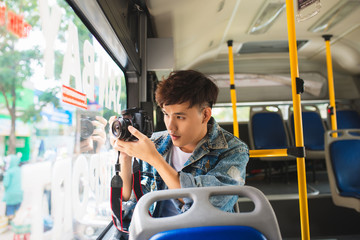 Asian male tourist taking video of the city using digital camera from the window of the bus