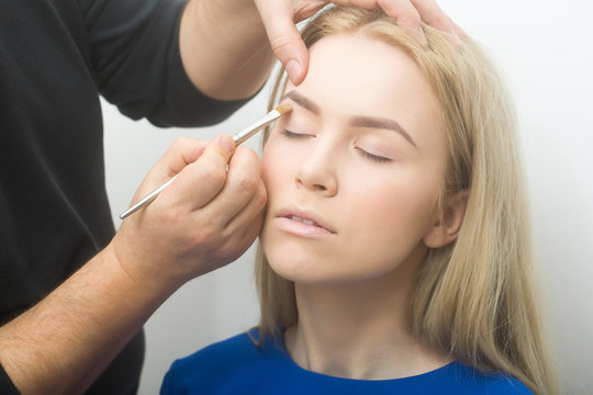 Hands applying concealer on girl eyelids with makeup brush