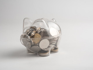 transparent see through piggy bank filled with coins on white background.