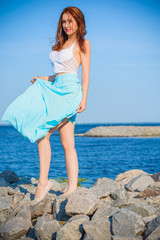 Redhead slim woman wearing tender pastel dress posing on a sea, fashionable woman walking on the shore. Young girl on a beach in a white tones. Pastel colors. The concept of femininity ad harmony