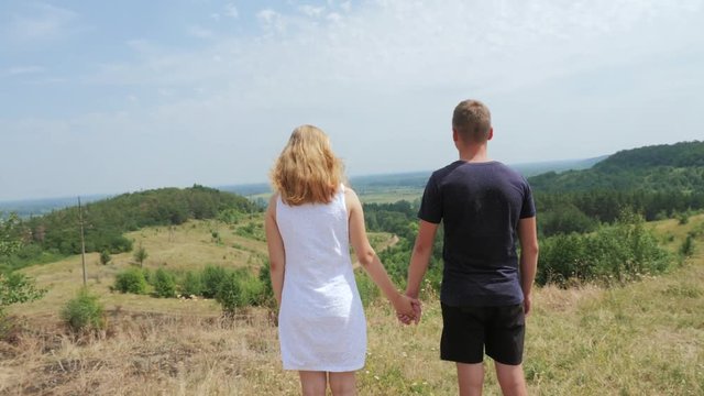 Couple man and woman standing on a hill looking into the distance. Steadicam shot. Summer Day.