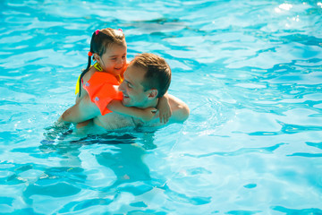 Young cheerful father and his little daughter in a swimming pool