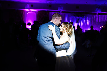 Newly married couple dancing on their wedding party with heavy smoke and multicolored lights on the background.