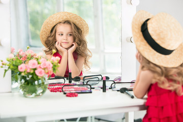 A little girl with cosmetics. She is in mother's bedroom, sitting near the mirror.