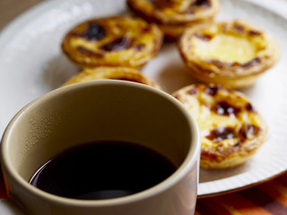 Softfocus custard tarts in a plate  and black coffee cup
