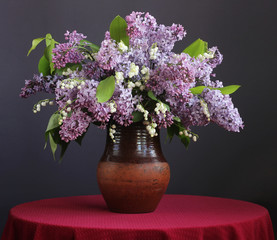 Bouquet of purple lilac and lilies in a clay jar