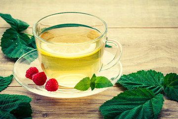 Glass cup of green tea with a saucer and the slice of lemon, leaves of mint, barriers and leaves of raspberries