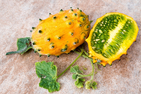 two fresh ripe kiwano with vine and leaves, Cucumis metuliferus, on ceramic background