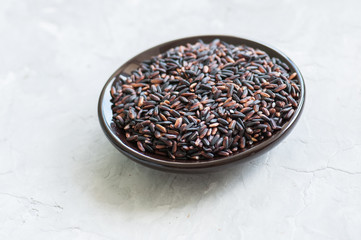 Brown rice in a plate on white stone background. Toned.