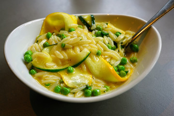 Dish of orzo pasta with zucchini, peas and lemon