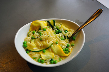 Dish of orzo pasta with zucchini, peas and lemon