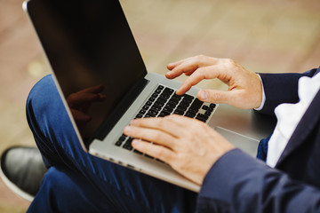 Male holding notebook on knees and typing text outdoors