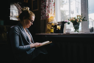 beautiful young woman reading interesting book while drinking tea at home, in cafe