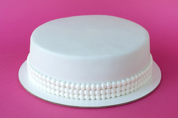 Cake baking with white mastic decorated with beads from pearls on pink background. Picture for a menu or a confectionery catalog.