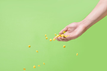 Flying yellow pills from hand in front of green background