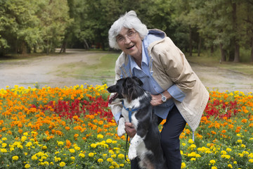 Naklejka na ściany i meble Senior woman hugging her dog in a park with blooming flowers