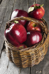 Harvest of red apples in wattled basket on a dark wooden background