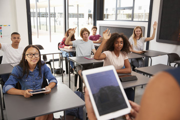 Teacher uses tablet in high school class, over shoulder view