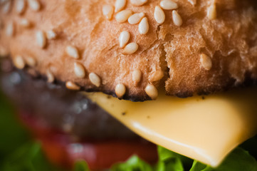 Hamburger on a black plate. Burger on a dark background. Bread roll for cheeseburger, cutlet, lettuce, tomatoes, cheese, greens, sauce, ketchup, sesame. American snacks