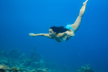 A brunette girl diving into blue sea water. Underwater photography of sport activity