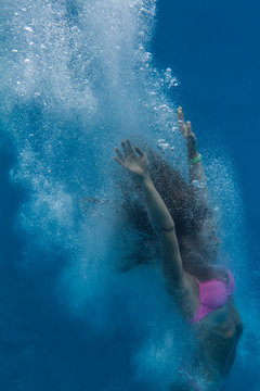 Drowning girl in pink bikini. A swimmer after jump underwater surrounded with air bubbles. Image on blue aquatic marine background