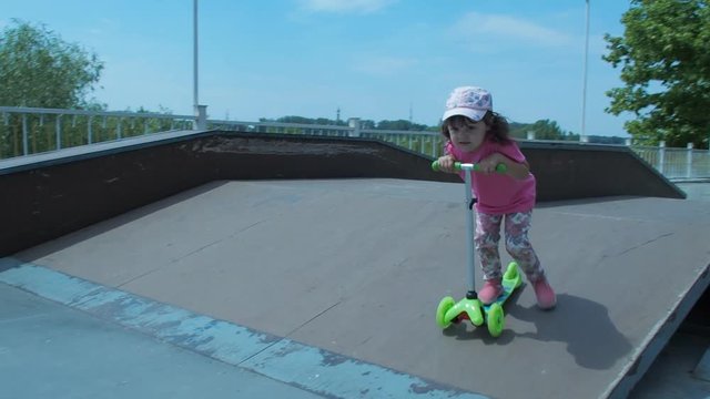 The child is riding a scooter. Little girl on a green scooter.