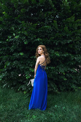 Obraz na płótnie Canvas Beautiful woman showing her back in blue dress near a big green bush