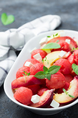 Fresh summer watermelon salad with feta, peach and mint on concrete, slate or stone background.