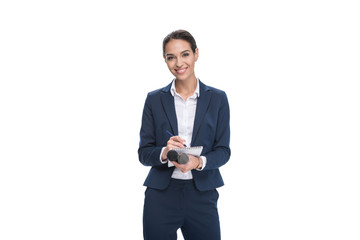 smiling female journalist in suit with microphone writing in notepad, isolated on white