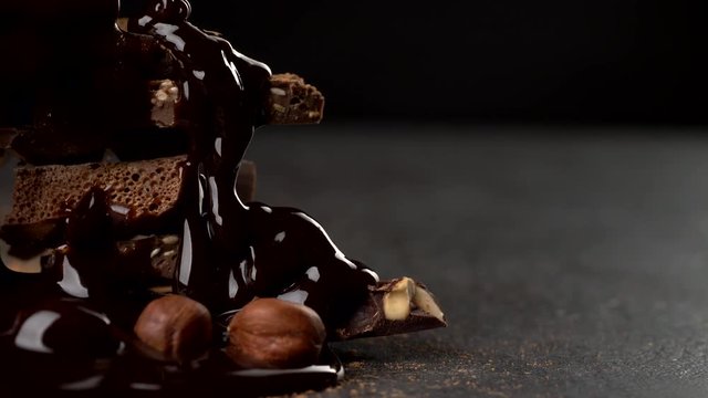 Pouring hot chocolate onto stack of various chocolate pieces and nuts in cocoa powder. Slider shot