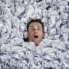 Business man with a great heap of crumpled papers. Swimming in paper ocean concept.