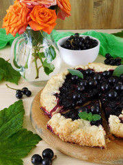 Galette with black currant on a wooden background. Berries and flowers in the background 