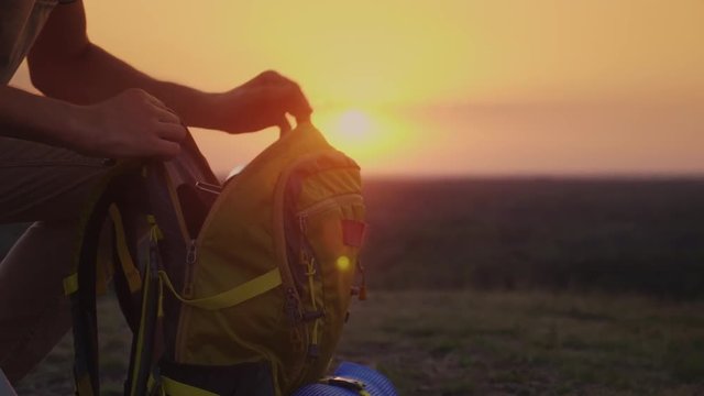 A man is packing his backpack at sunset. Preparing for a trip or trekking