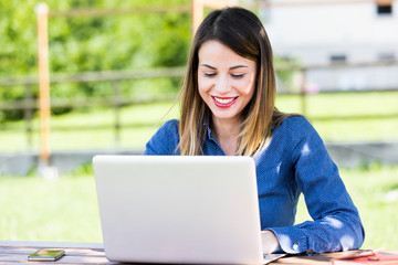 Beautiful, smiling woman using laptop outdoors