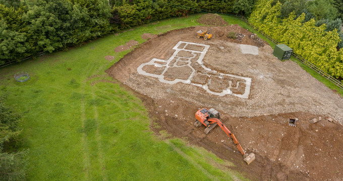 Aerial birds eye view of a new build concrete foundation for a home in the countryside. Green filed with machinery digger and dumper truck.