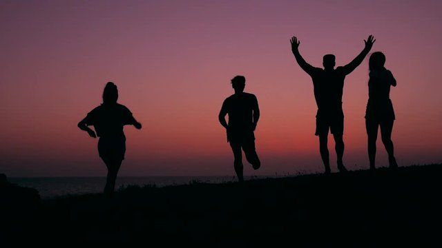 Group of Four Young Mixed Race Teenage Hipsters Run To Cliff On The Beach At Amazing Sunset. HD Slowmotion Carefree Lifestyle Silhouette Footage.